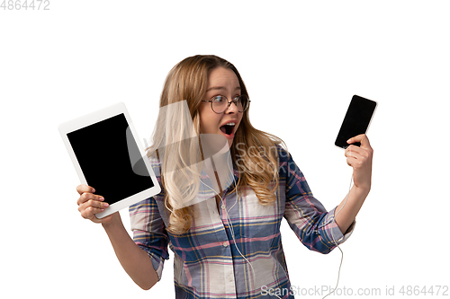 Image of Emotional caucasian woman using gadgets on white studio background, technologies. Crazy happy shows tablet and smartphone