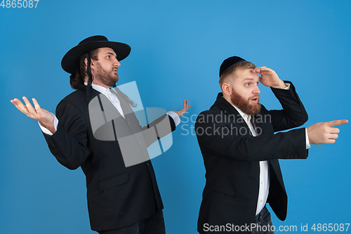 Image of Portrait of a young orthodox jewish men isolated on blue studio background, meeting the Passover, astonished