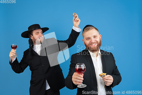 Image of Portrait of a young orthodox jewish men isolated on blue studio background, meeting the Passover, eating Aman\'s ears with wine