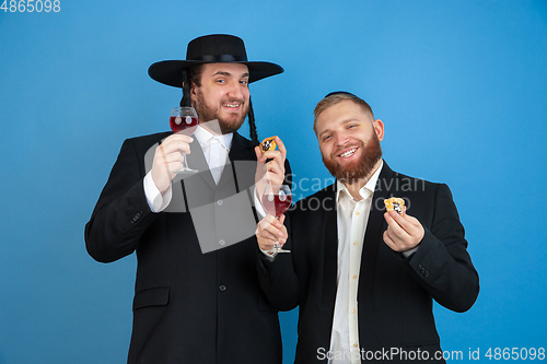 Image of Portrait of a young orthodox jewish men isolated on blue studio background, meeting the Passover, eating Aman\'s ears with wine