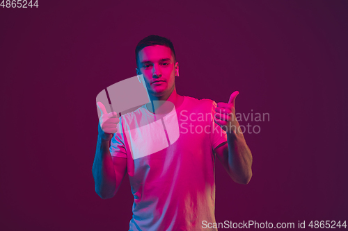 Image of Caucasian man\'s portrait isolated on pink-purple studio background in neon light, using wireless earphones