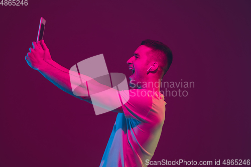 Image of Caucasian man\'s portrait isolated on pink-purple studio background in neon light, using tablet