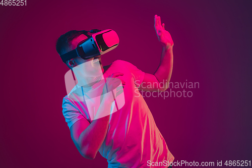 Image of Caucasian man\'s portrait isolated on pink-purple studio background in neon light, playing with VR-headset