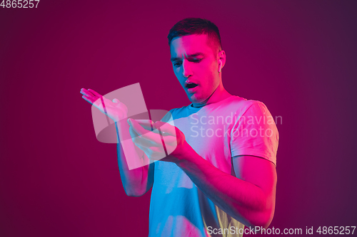 Image of Caucasian man\'s portrait isolated on pink-purple studio background in neon light, with smartphone and earphones