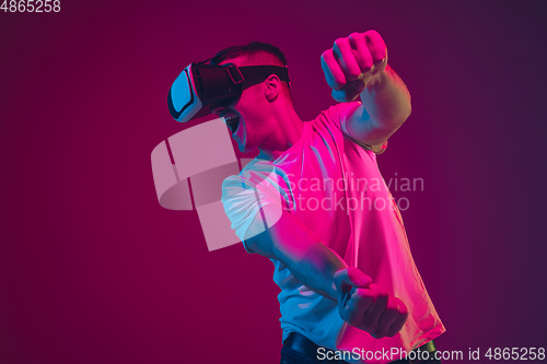 Image of Caucasian man\'s portrait isolated on pink-purple studio background in neon light, playing with VR-headset