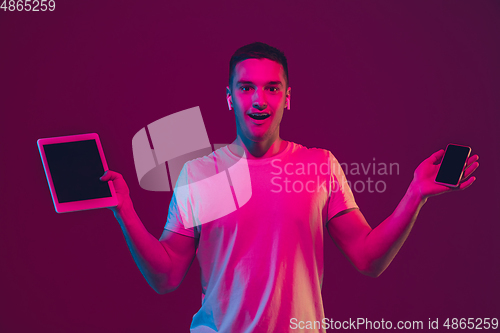 Image of Caucasian man\'s portrait isolated on pink-purple studio background in neon light, using tablet