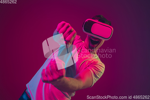 Image of Caucasian man\'s portrait isolated on pink-purple studio background in neon light, playing with VR-headset