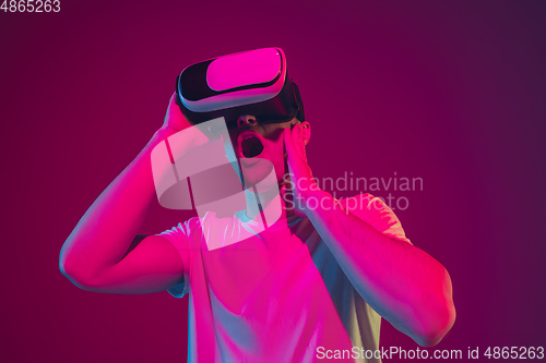 Image of Caucasian man\'s portrait isolated on pink-purple studio background in neon light, playing with VR-headset