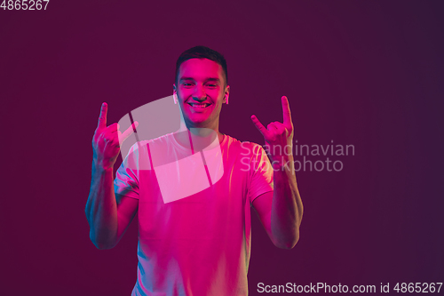 Image of Caucasian man\'s portrait isolated on pink-purple studio background in neon light, using wireless earphones