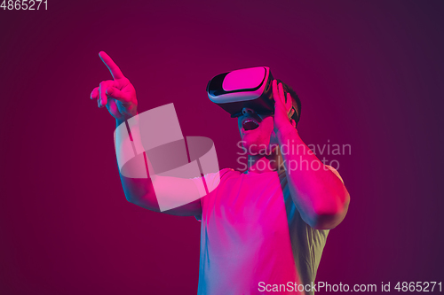 Image of Caucasian man\'s portrait isolated on pink-purple studio background in neon light, playing with VR-headset