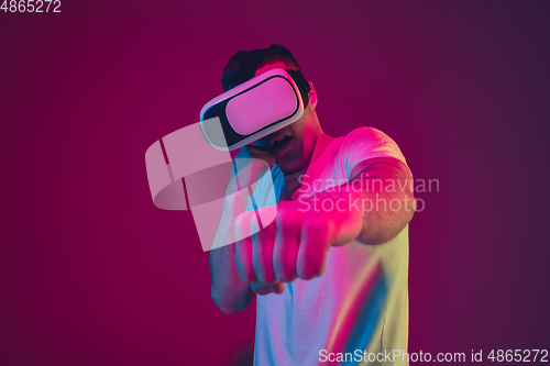 Image of Caucasian man\'s portrait isolated on pink-purple studio background in neon light, playing with VR-headset