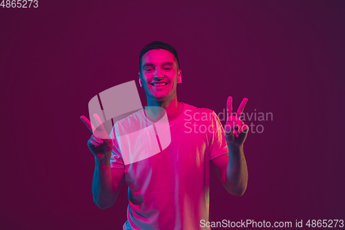 Image of Caucasian man\'s portrait isolated on pink-purple studio background in neon light, using wireless earphones