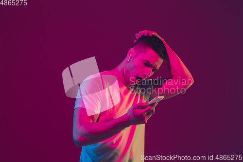 Image of Caucasian man\'s portrait isolated on pink-purple studio background in neon light, using tablet
