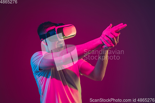 Image of Caucasian man\'s portrait isolated on pink-purple studio background in neon light, playing with VR-headset