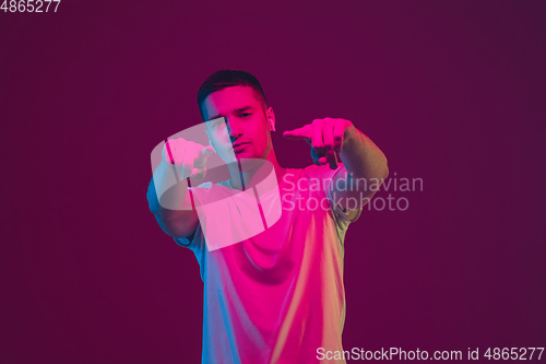 Image of Caucasian man\'s portrait isolated on pink-purple studio background in neon light, using wireless earphones