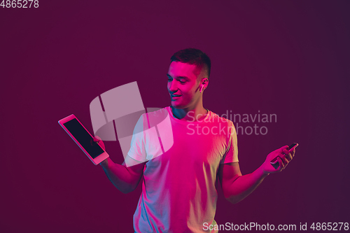 Image of Caucasian man\'s portrait isolated on pink-purple studio background in neon light, using tablet