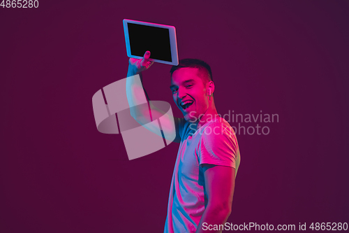 Image of Caucasian man\'s portrait isolated on pink-purple studio background in neon light, using tablet