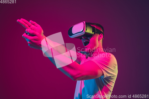 Image of Caucasian man\'s portrait isolated on pink-purple studio background in neon light, playing with VR-headset