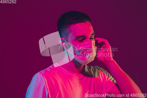 Image of Caucasian man\'s portrait isolated on pink-purple studio background in neon light, wearing face mask