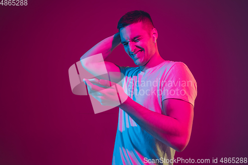Image of Caucasian man\'s portrait isolated on pink-purple studio background in neon light, with smartphone and earphones