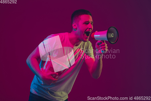 Image of Caucasian man\'s portrait isolated on pink-purple studio background in neon light, using speaker