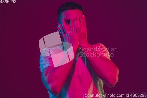 Image of Caucasian man\'s portrait isolated on pink-purple studio background in neon light, using wireless earphones