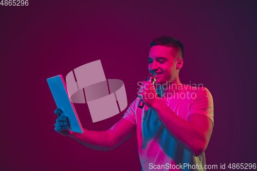 Image of Caucasian man\'s portrait isolated on pink-purple studio background in neon light, using tablet