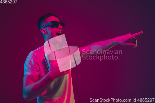 Image of Caucasian man\'s portrait isolated on pink-purple studio background in neon light, wearing 3D-cinema eyewear