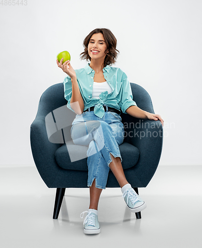 Image of happy woman with green apple sitting in armchair