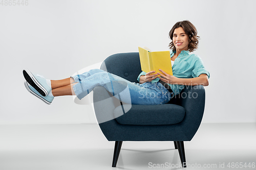 Image of happy young woman in armchair reading book