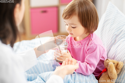 Image of doctor giving medicine to sick girl in bed at home