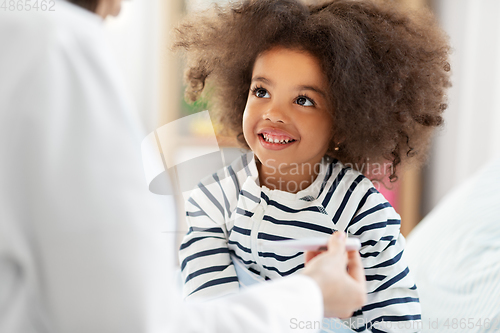 Image of doctor showing thermometer to smiling sick girl