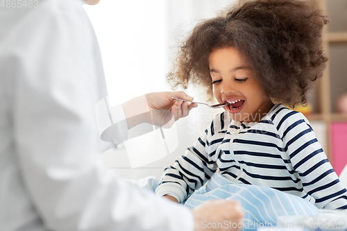 Image of doctor giving medicine to sick girl in bed at home