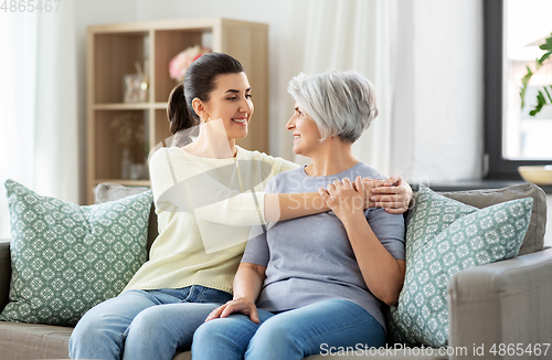 Image of senior mother with adult daughter hugging at home