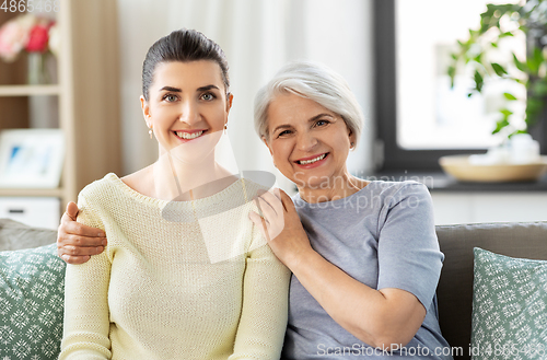 Image of senior mother with adult daughter hugging at home