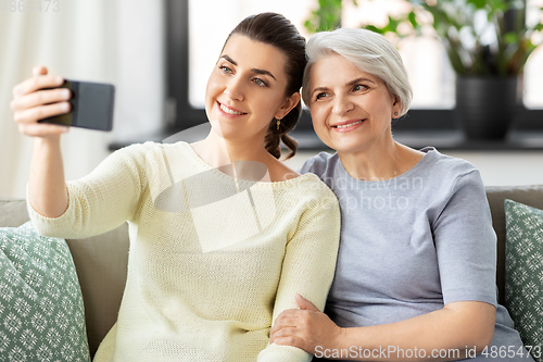 Image of senior mother with daughter taking selfie at home