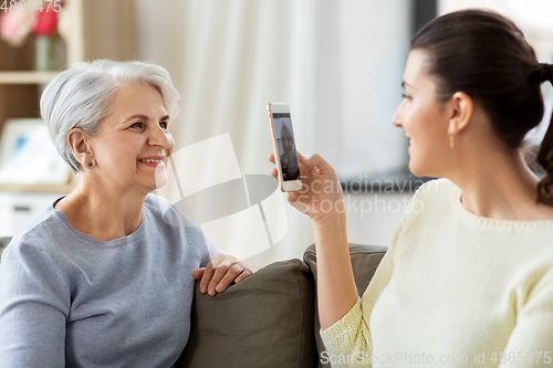 Image of adult daughter photographing senior mother at home