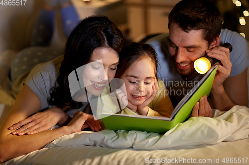 Image of happy family reading book in bed at night at home