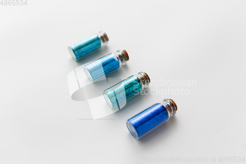 Image of blue glitters in bottles over white background