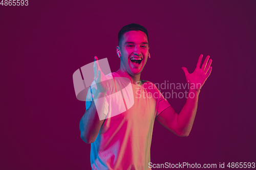 Image of Caucasian man\'s portrait isolated on pink-purple studio background in neon light, using wireless earphones
