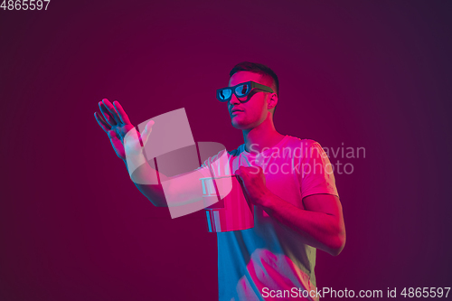 Image of Caucasian man\'s portrait isolated on pink-purple studio background in neon light, wearing 3D-cinema eyewear