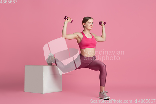 Image of Beautiful young female athlete practicing on pink studio background, monochrome portrait