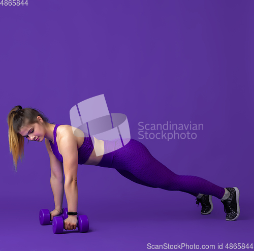 Image of Beautiful young female athlete practicing on purple studio background, monochrome portrait