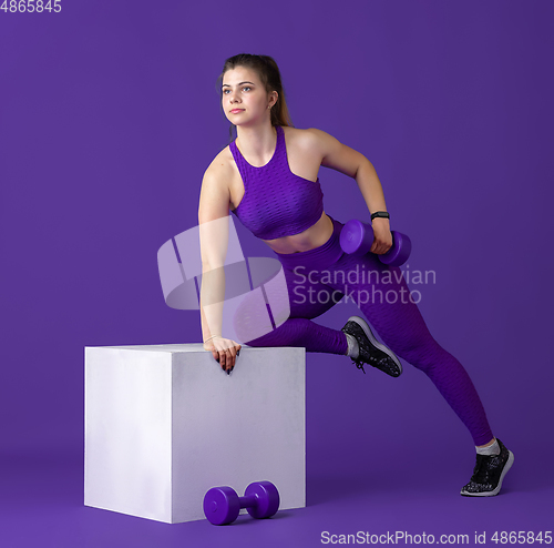 Image of Beautiful young female athlete practicing on purple studio background, monochrome portrait