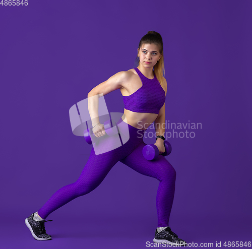 Image of Beautiful young female athlete practicing on purple studio background, monochrome portrait