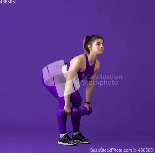 Image of Beautiful young female athlete practicing on purple studio background, monochrome portrait