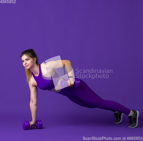 Image of Beautiful young female athlete practicing on purple studio background, monochrome portrait