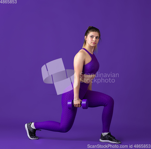 Image of Beautiful young female athlete practicing on purple studio background, monochrome portrait