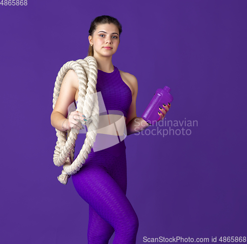 Image of Beautiful young female athlete practicing on purple studio background, monochrome portrait