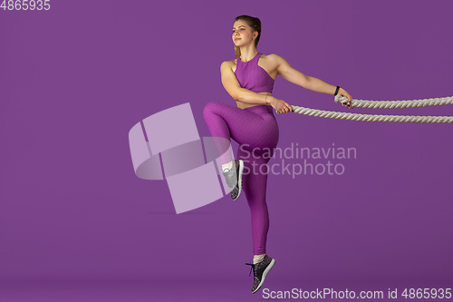 Image of Beautiful young female athlete practicing on purple studio background, monochrome portrait